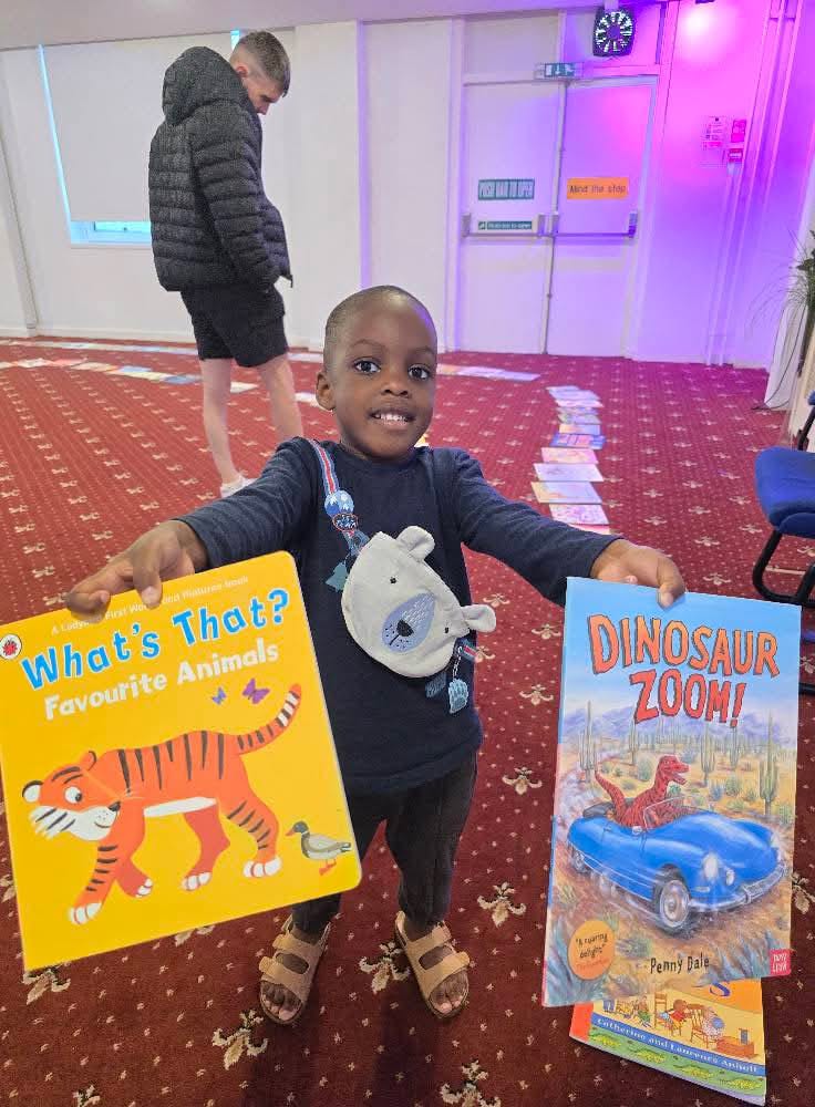 Child holding children's books at community event with purple lighting